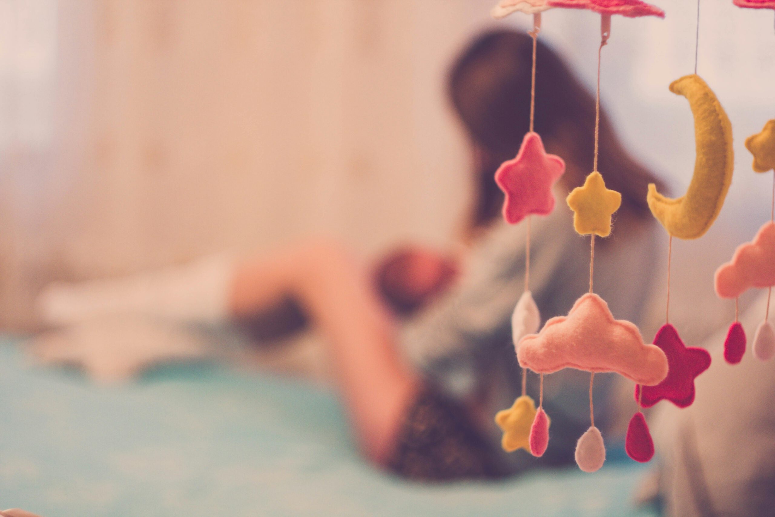 A mother cradling her baby next to a dreamy cloud and star mobile in a soft-focus bedroom setting.